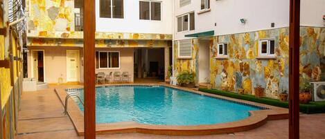 Una piscina con plataforma de baldosas, rodeada de edificios con balcones y ventanas.