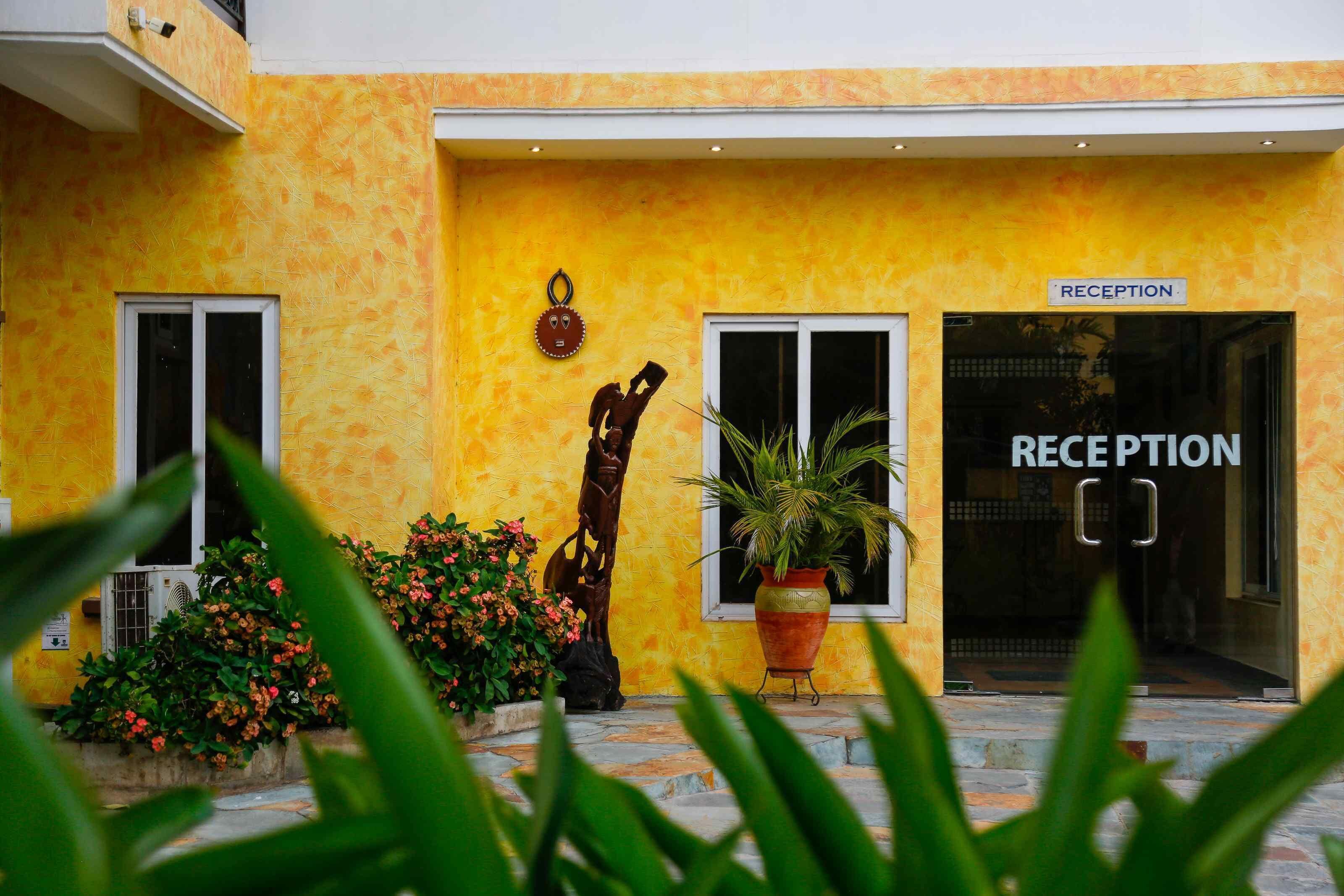 A reception area with a yellow wall, a reception sign, and a potted plant.