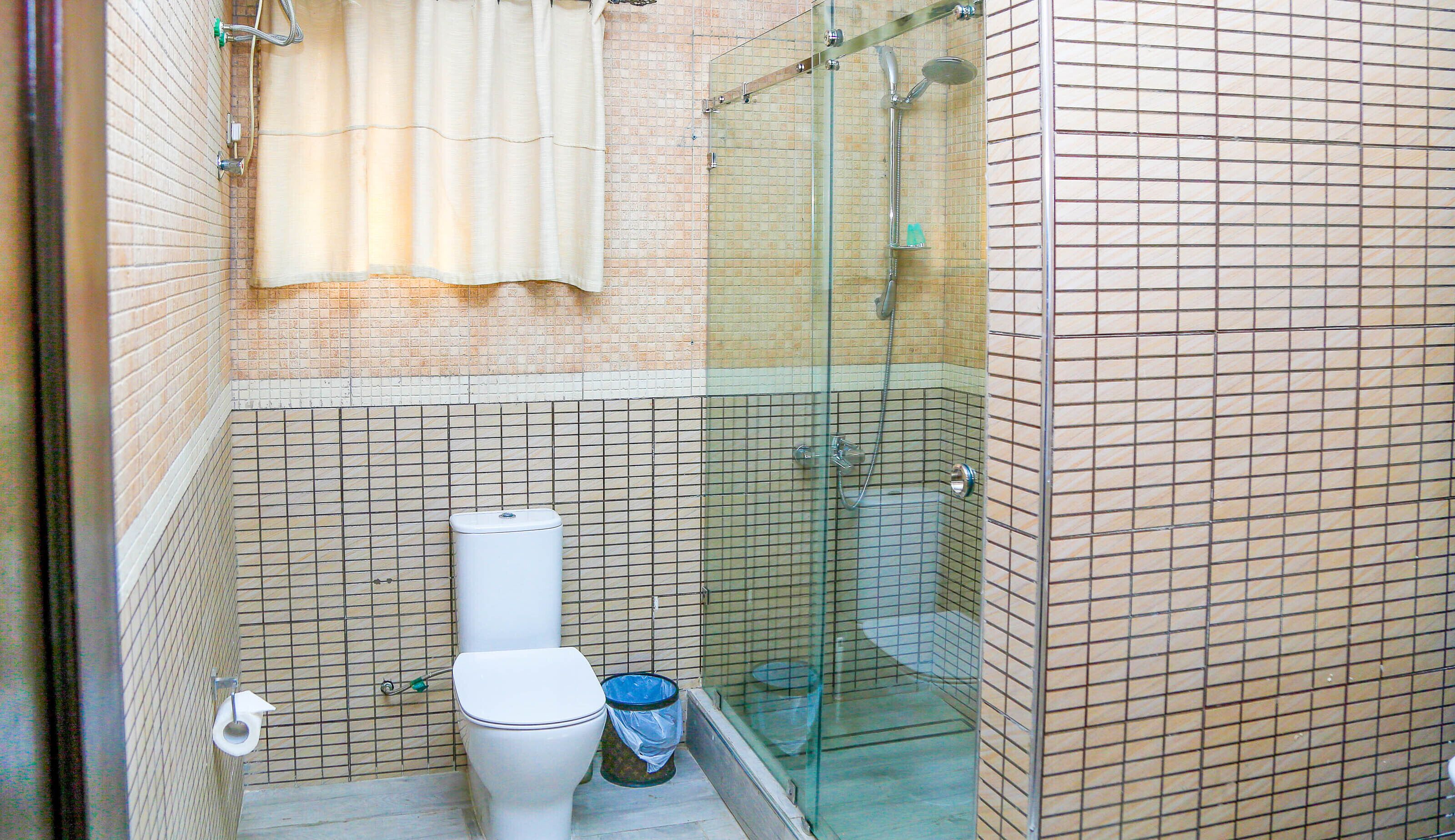 A small bathroom with a toilet, a shower, and a trash bin.