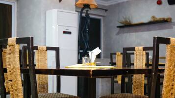 Un comedor con una mesa lista para dos, con sillas de mimbre y una lámpara de mesa.