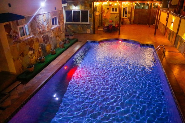 A swimming pool with a stone wall and a small garden area with potted plants.