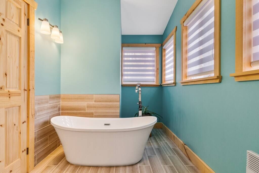 Un baño con una bañera independiente, puerta de madera y paredes azul claro.