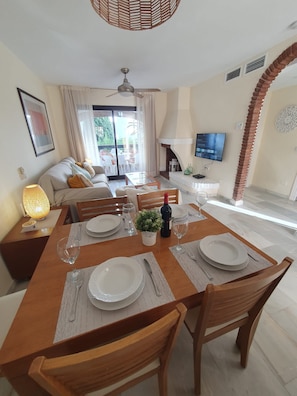 A dining area with a wooden table set for four, a sofa, a TV, and a fireplace.