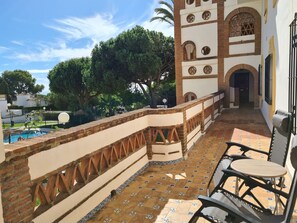 A terrace with a pool, outdoor seating, and a view of a building with arches and a tower.