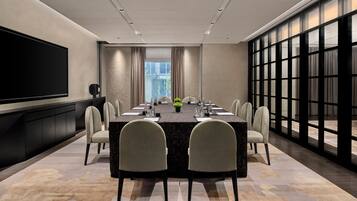 A conference room with a long table, chairs, a flat-screen TV, and a large window.