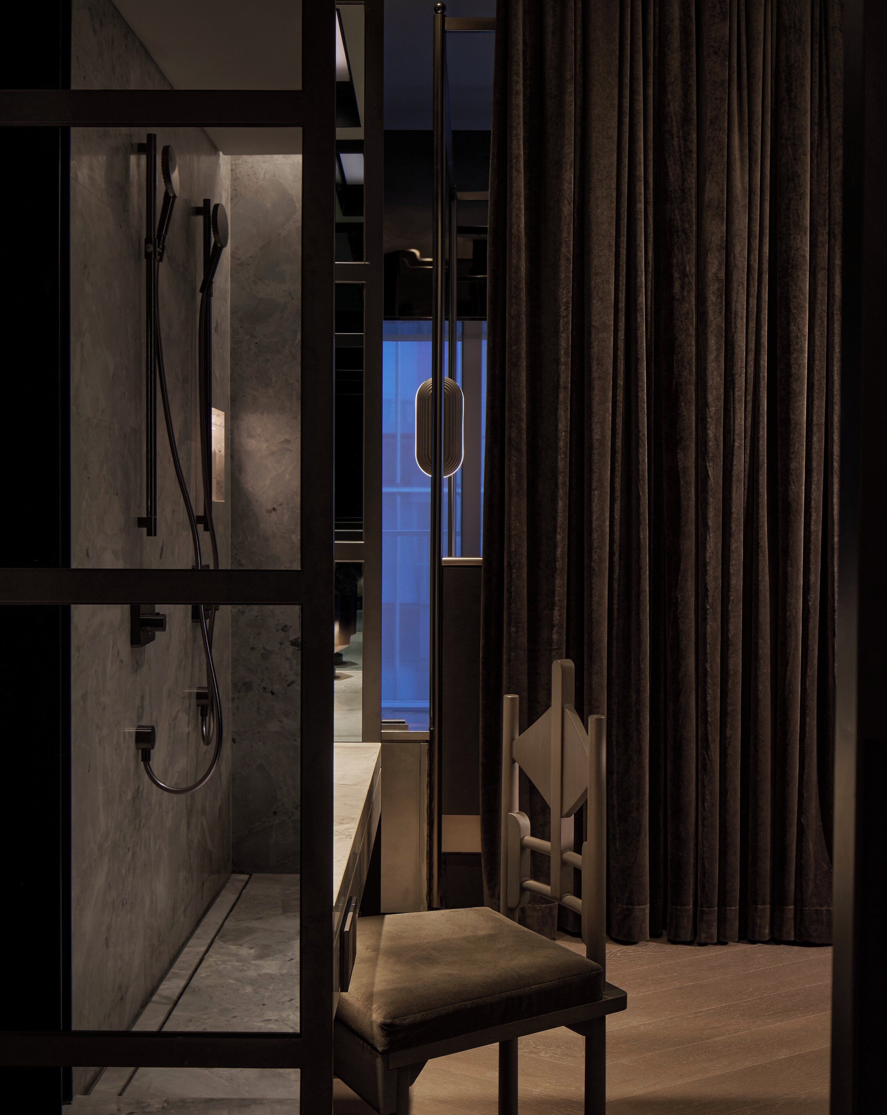 A modern bathroom with a shower, a chair, and a view of a cityscape through a window.