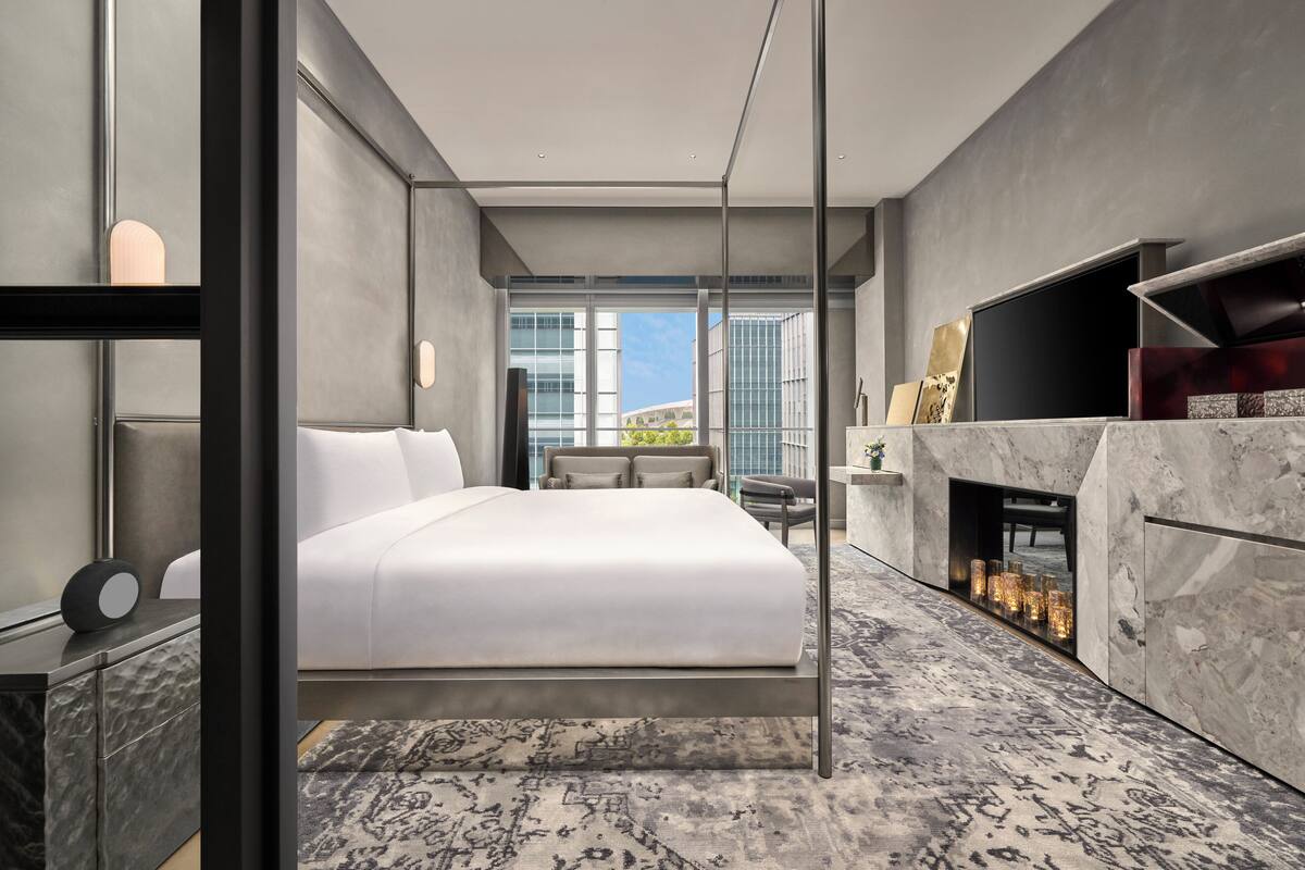 A modern hotel room with a large bed, a fireplace, and a view of the city.