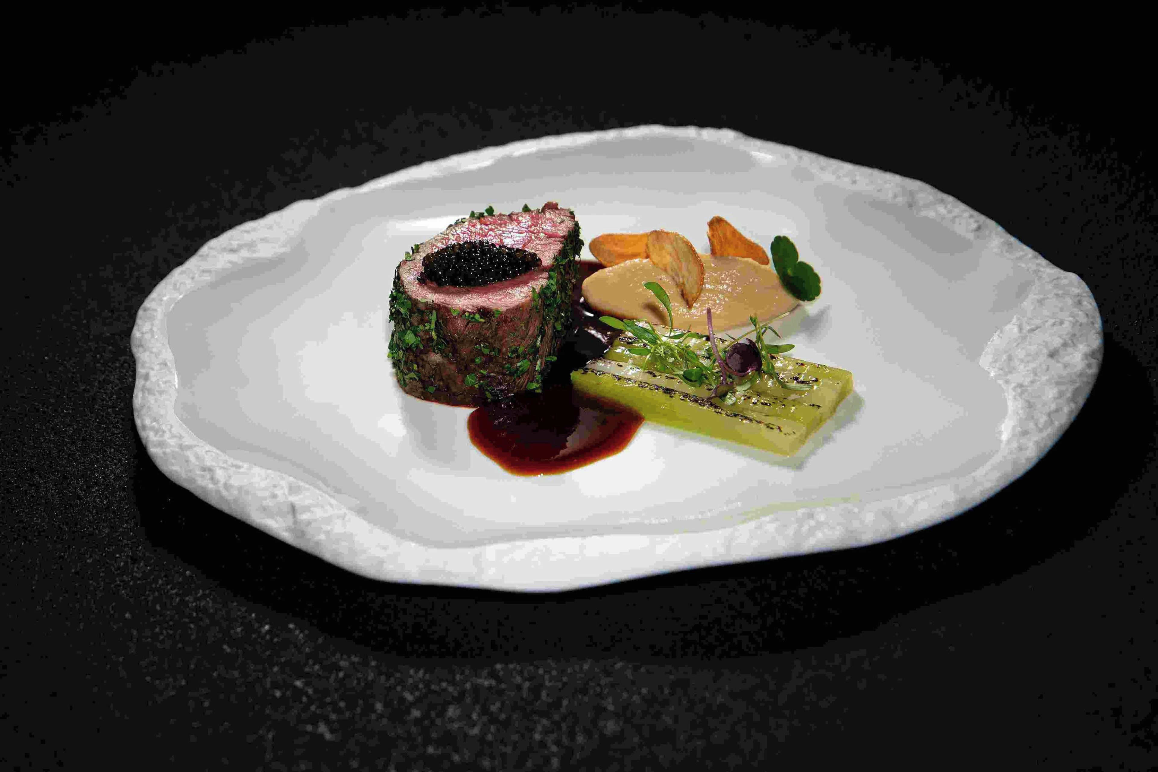 A plated dish with a piece of meat, a green vegetable, and a sauce.