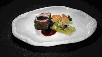 A plated dish with a piece of meat, a green vegetable, and a sauce.