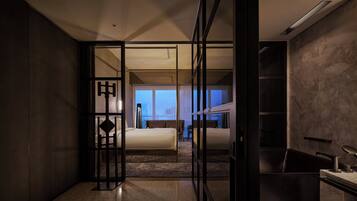A modern hotel room with a glass partition, a bed, a desk, and a view of the cityscape.