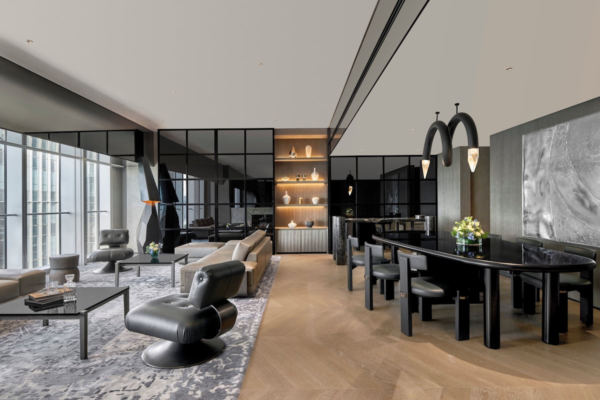 A modern living room with a black dining table, leather sofas, and a large window.