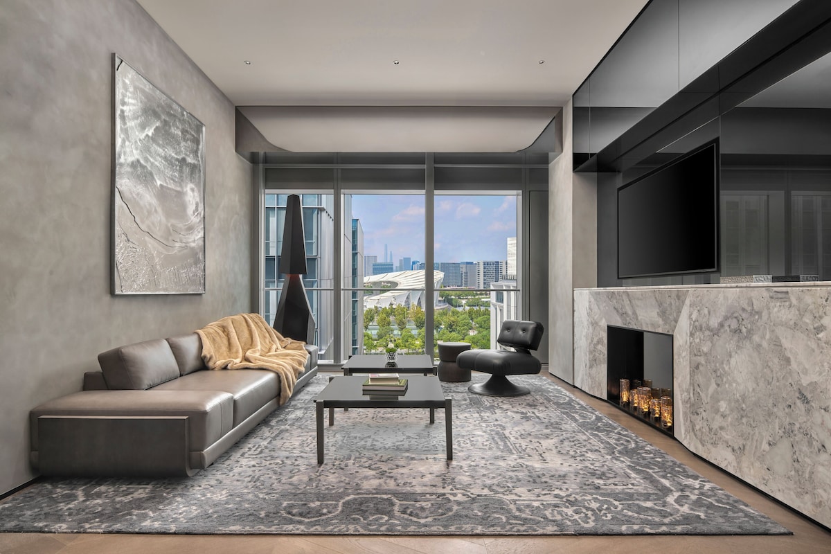 A modern living room with a sofa, coffee table, and fireplace, featuring a city view through large windows.