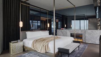 A modern bedroom with a four-poster bed, a marble fireplace, and a city view through large windows.