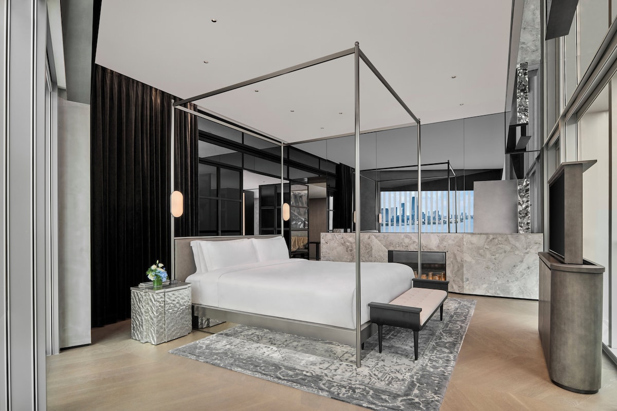 A modern bedroom with a four-poster bed, a marble fireplace, and a city view.