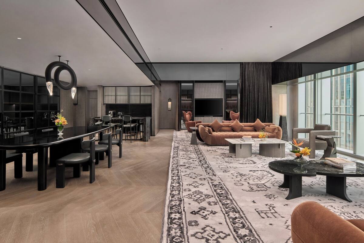 A modern living room with a large sofa, a dining area with a black table, and a TV mounted on the wall.