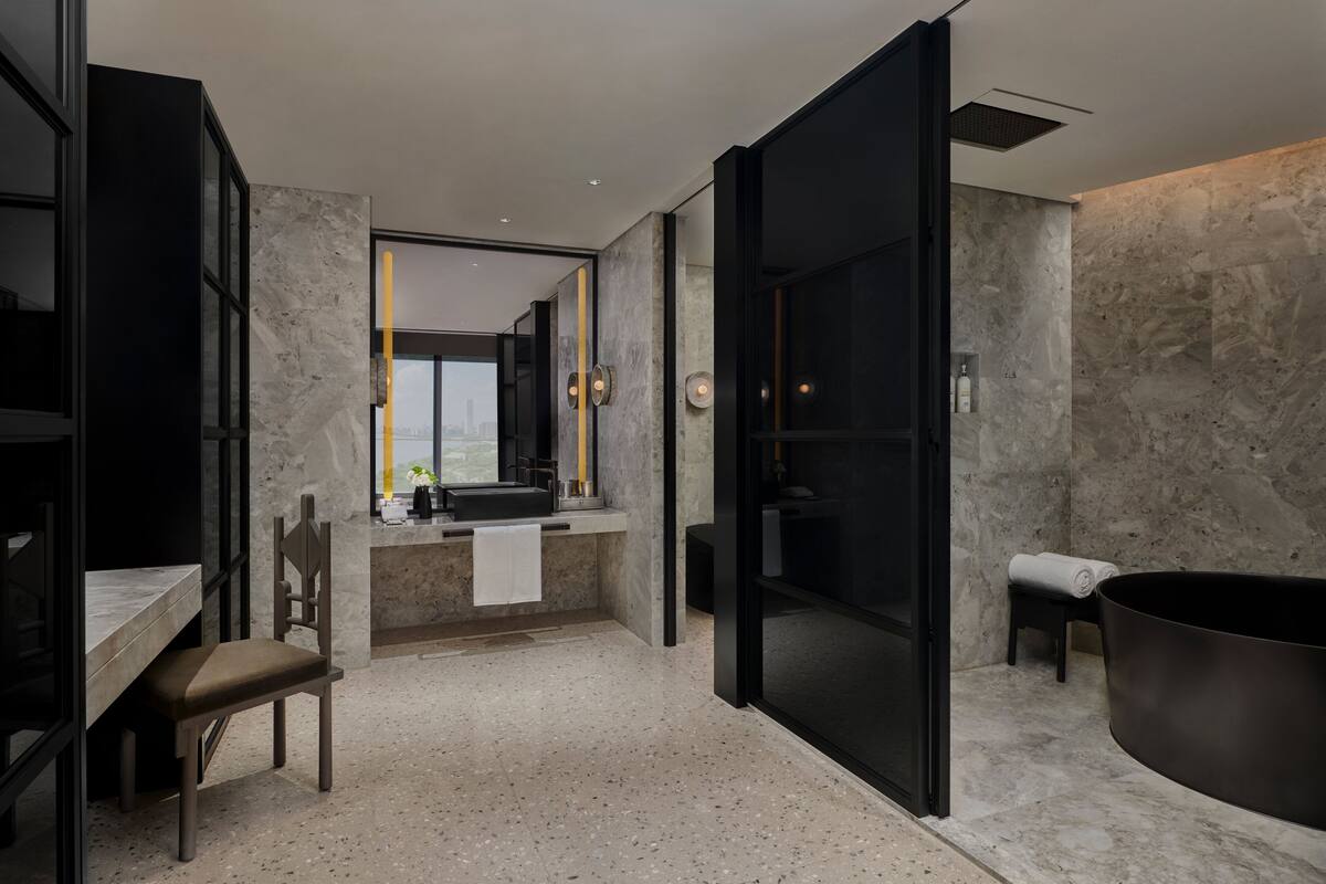 A modern bathroom with a large bathtub, a glass shower enclosure, and a seating area with a chair and table.