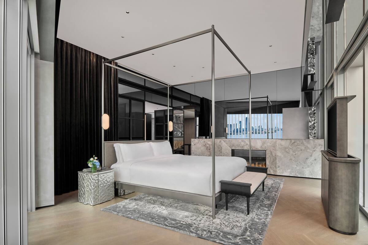 A modern bedroom with a four-poster bed, a marble fireplace, and a city view.