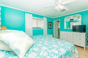 A bedroom with a bed, a dresser, a television, and a ceiling fan.