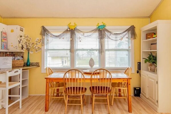 A dining area with a wooden table and chairs, a window with a decorative net, and a white cabinet with shelves. - SunRay! 2nd Row, Ocean View, Walk to Beach, 3 Bedrooms, 2 Bathrooms, Family Home (Surfside Beach)