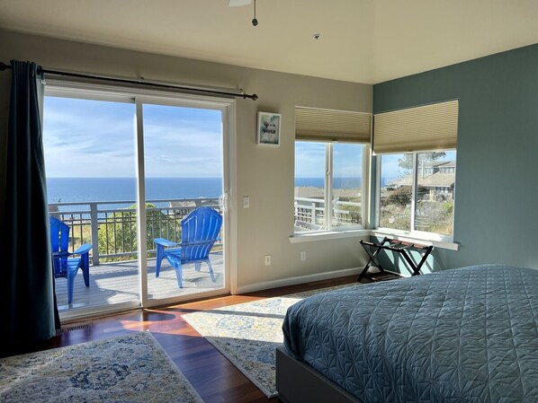Relax in this serene bedroom with a large bed, sliding glass door to a balcony with ocean views, and a desk for work or relaxation.