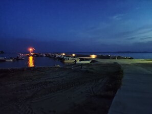 Boats are moored along the water's edge, with a sandy beach and paved walkway nearby.