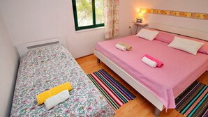 Un dormitorio con una cama individual, una cama más pequeña, una mesita de noche, una lámpara y una ventana con cortinas.
