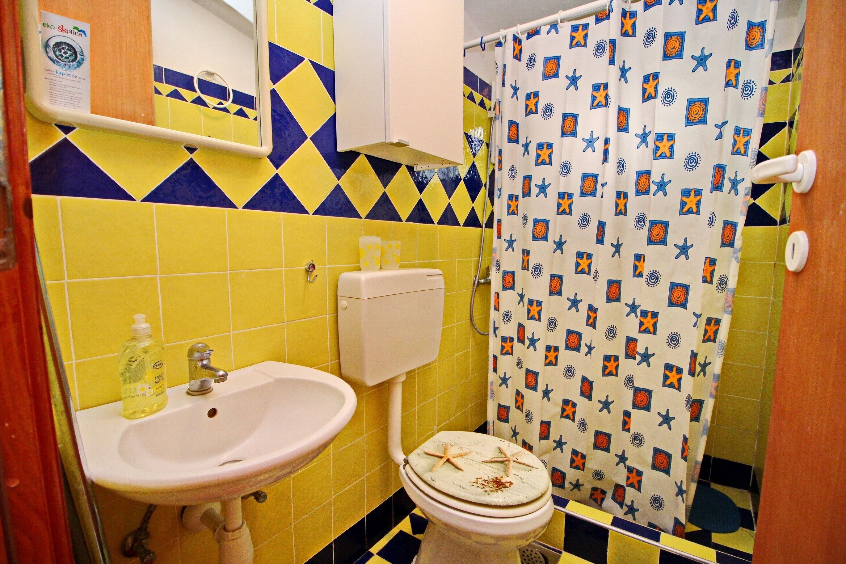 A bathroom with yellow and blue tiles, a white sink, a toilet, and a shower curtain with star patterns.