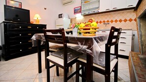 Una cocina con una mesa de comedor, sillas, un televisor y una cesta de frutas.
