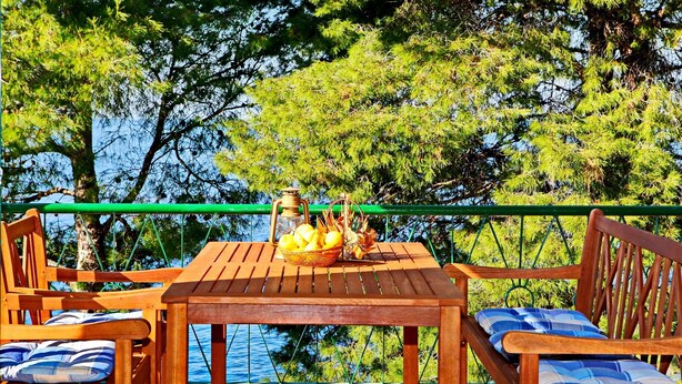 A wooden table and chairs with a basket of fruit and a lantern on the table, overlooking a body of water and trees. - Apartments Sunset - Two Bedroom Apartment with Terrace and Sea View (Blato)