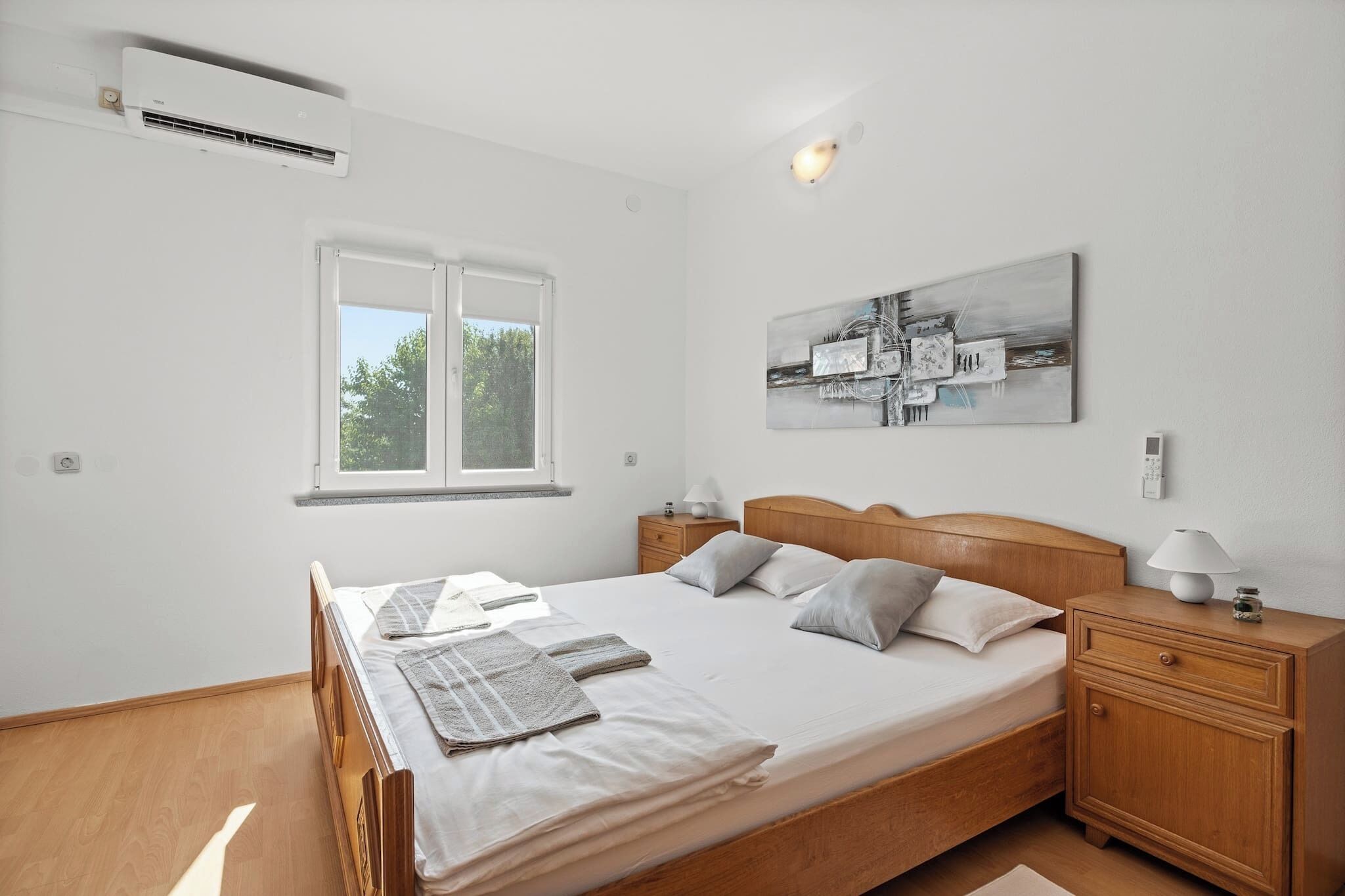 Quarto com cama, mesas de cabeceira, um criado-mudo, janela e ar condicionado fixado na parede.
