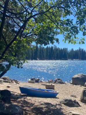 A boat on a sandy beach with a forest and a body of water in the background.