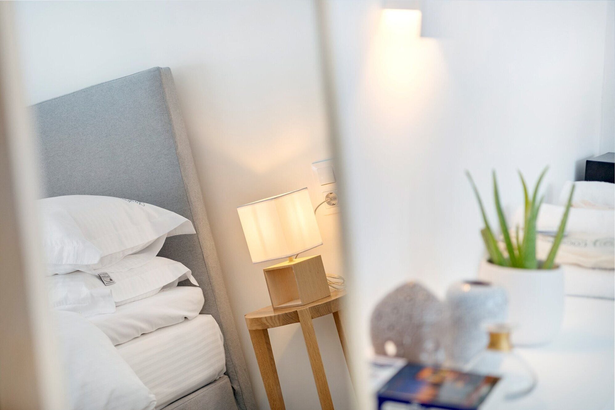 A neatly made bed with white linens, a bedside lamp, and a small wooden nightstand with a lamp.