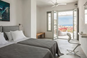 Relax in a serene space with a large bed, a small bench, and a chair, offering a view of the sea from the balcony.
