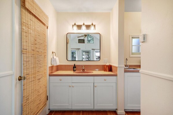 Une salle de bain avec une porte en bois, un meuble-lavabo blanc avec un miroir et un évier.