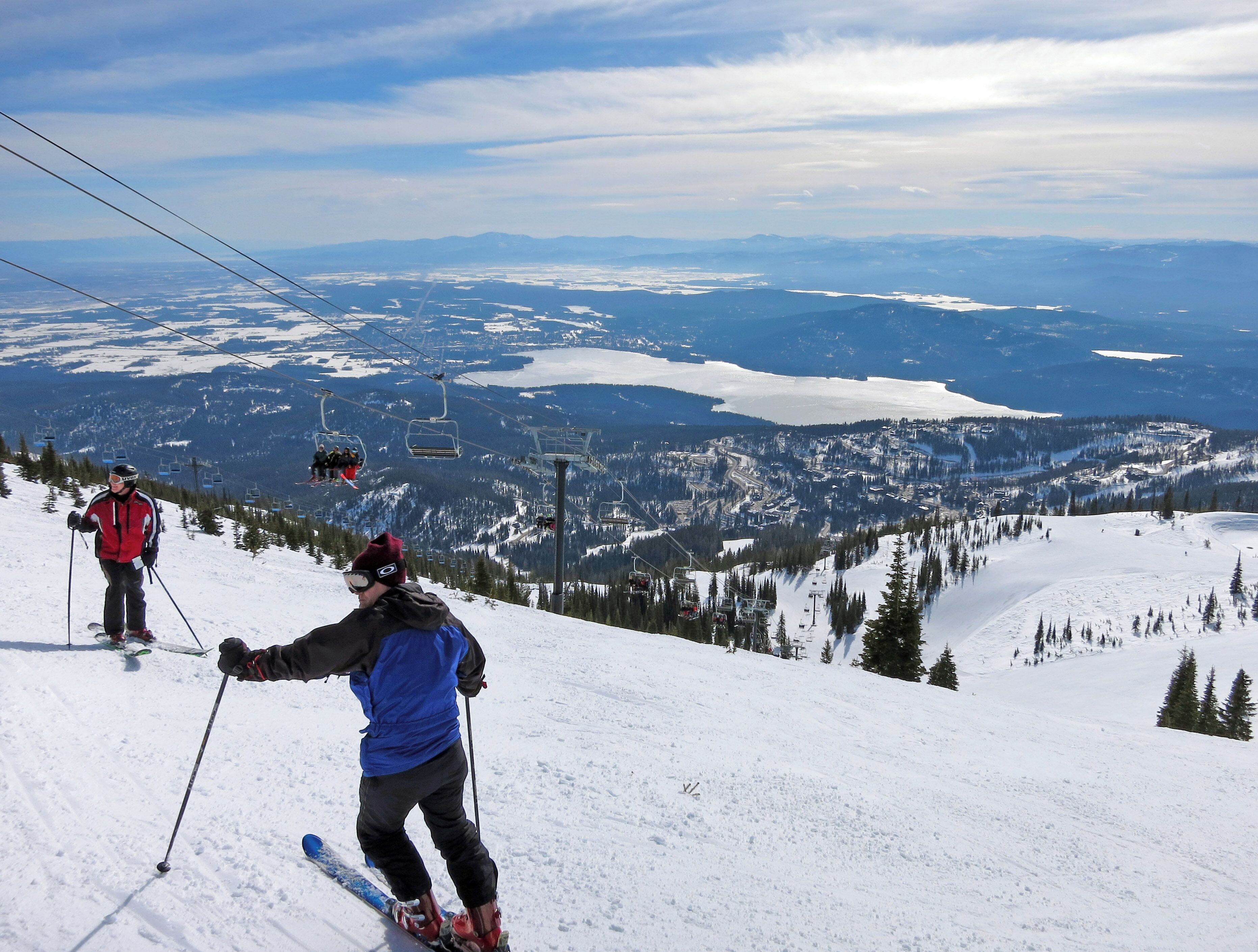 Une piste de ski avec des skieurs, un télésiège et une vue panoramique sur un paysage montagneux.
