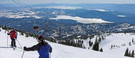 Une piste de ski avec des skieurs, un télésiège et une vue panoramique sur un paysage montagneux.