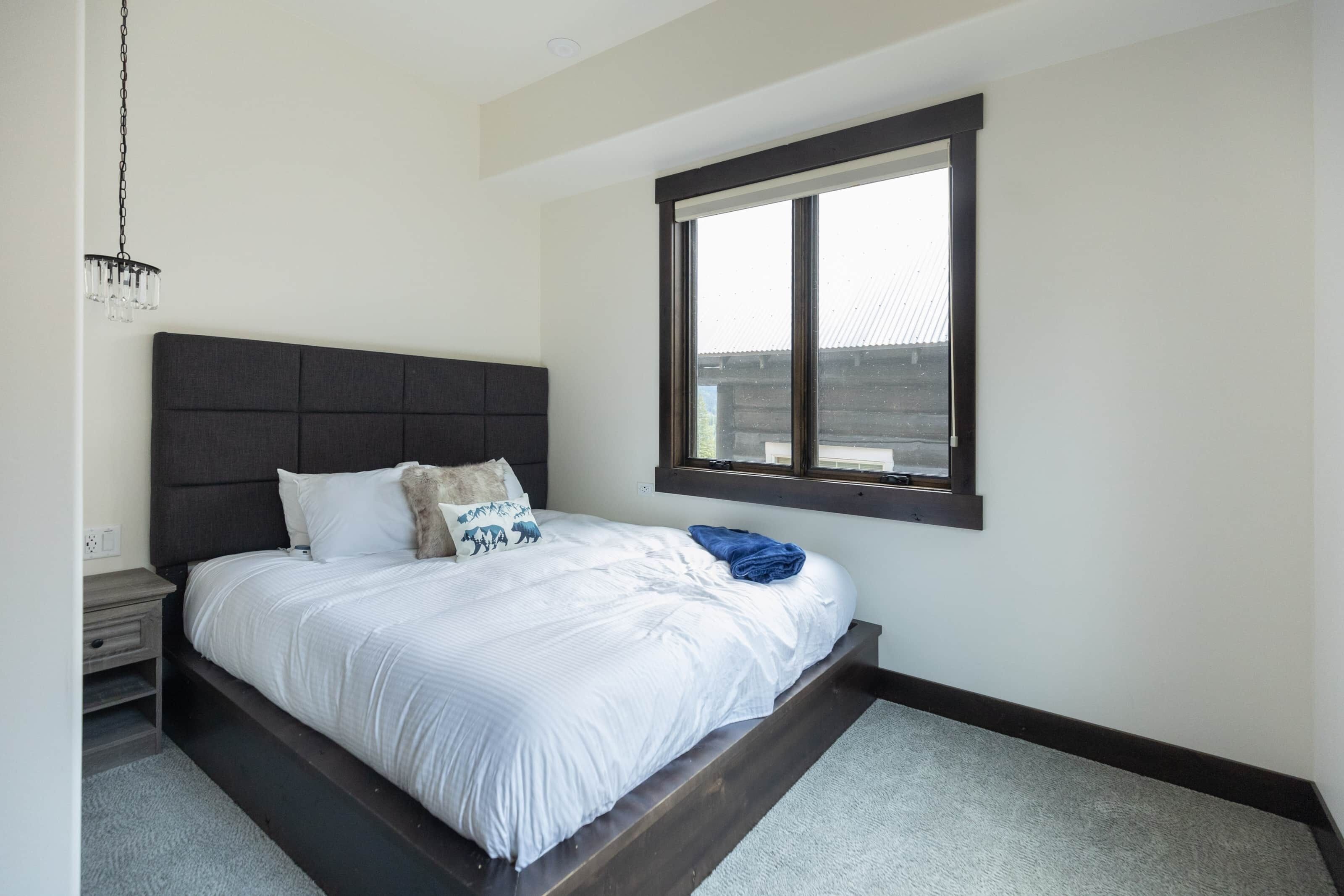 A bedroom with a bed, a nightstand, a window, and a chandelier.