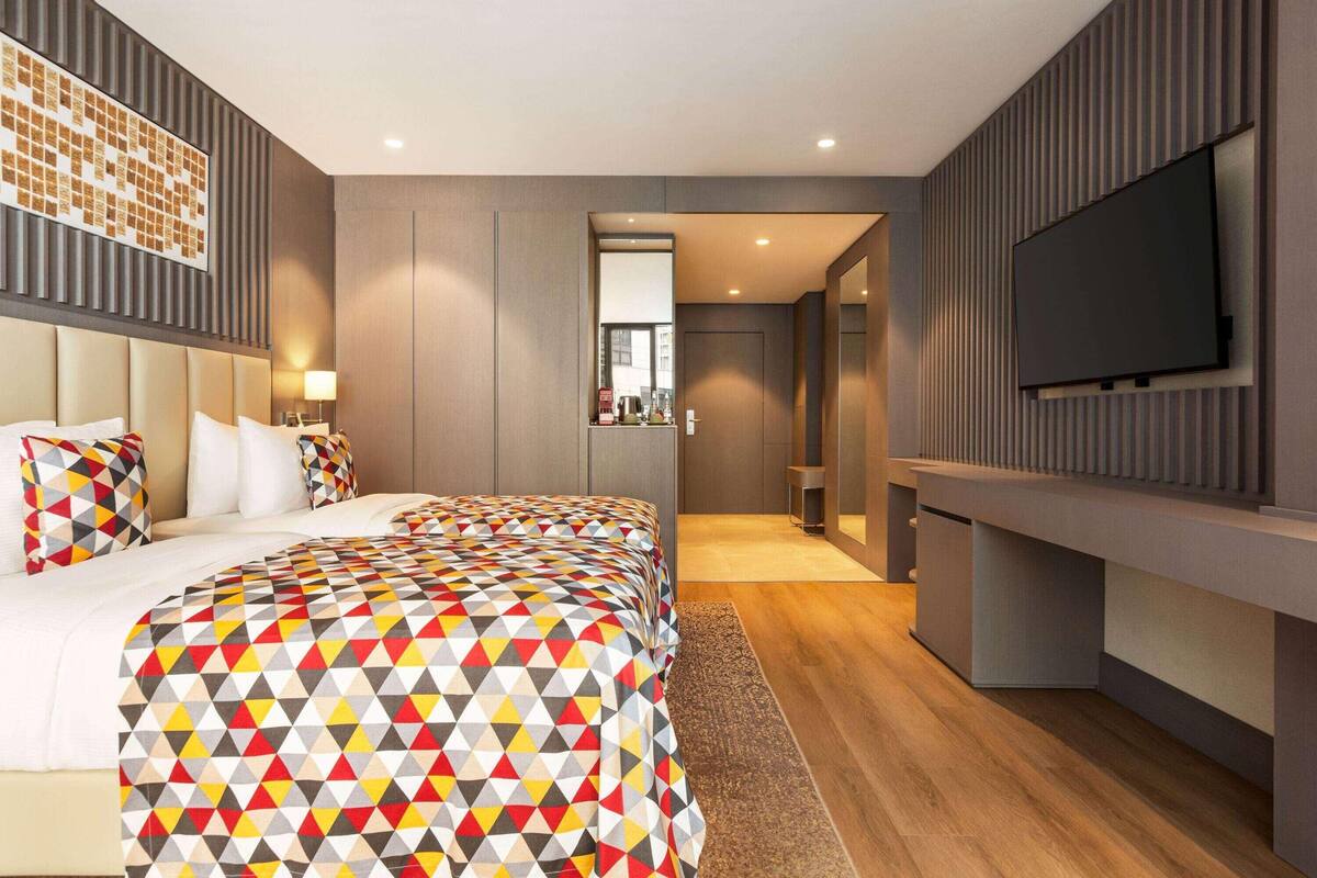 Ein modernes Hotelzimmer mit einem großen Bett, einem an der Wand montierten Fernseher und einem Arbeitsbereich.