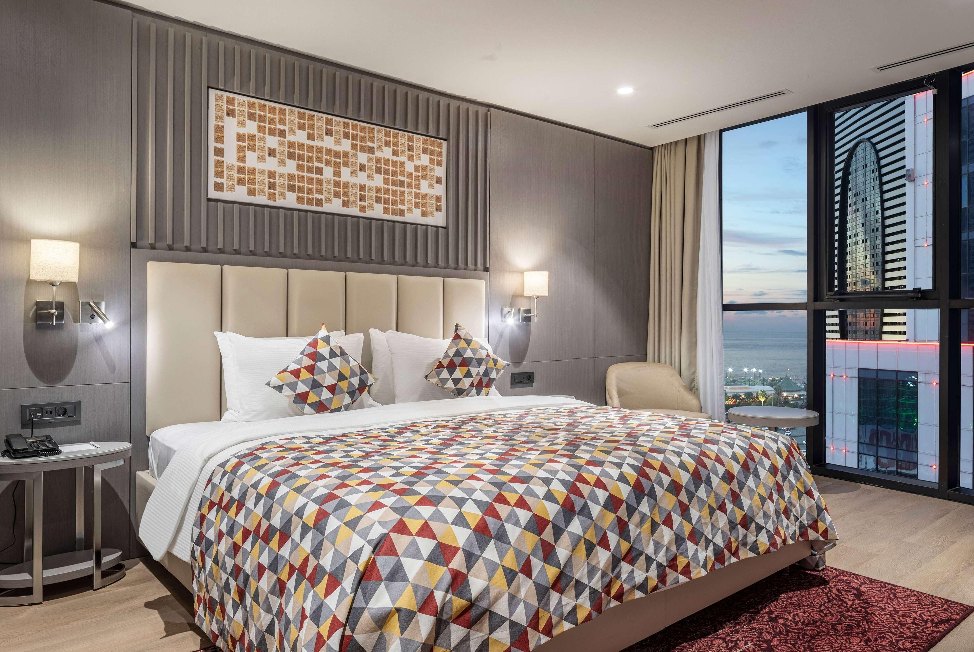 Een moderne hotelkamer met een groot bed, stadszicht en een bed met een patroon.