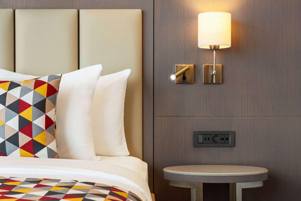 Una habitación de hotel con una cama, una lámpara de pared y una mesita.