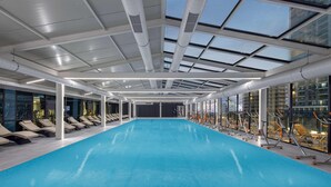 Een binnenzwembad met dakraam, fitnessapparatuur en lounge stoelen.