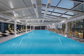 Une piscine intérieure dotée d’un toit en verre permettant de profiter de la lumière naturelle, ainsi que d’équipements de musculation et de chaises longues.