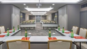 Een vergaderruimte met meerdere tafels, stoelen en een projector aan het plafond.