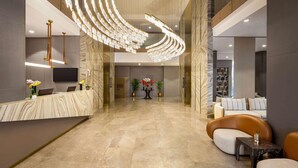 Een moderne lobby met een marmeren receptiebalie, een ronde plafondlamp en een zithoek met banken en een salontafel.