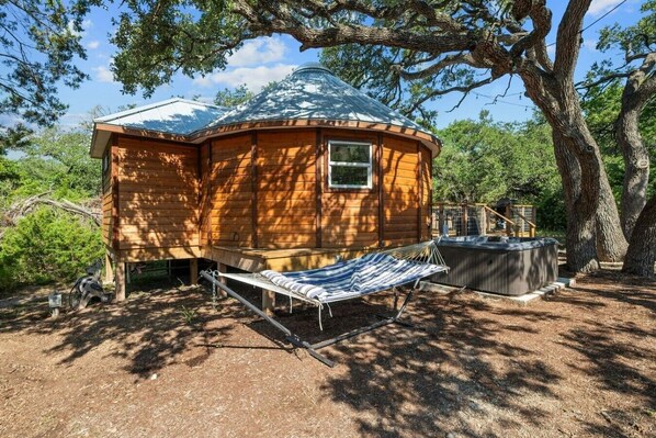 Uma cabana de madeira com telhado abobadado, uma rede e uma banheira de hidromassagem.