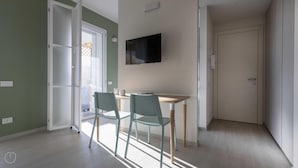A room with a dining table and chairs, a TV mounted on the wall, and a door leading to another room. - Italianway - Flavio Gioia 5 (Milan)