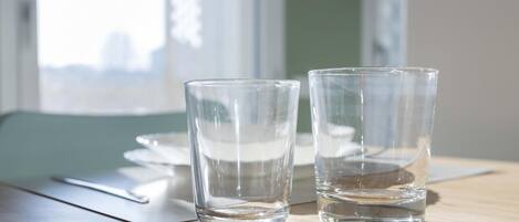 Two clear glasses on a wooden table with a napkin and a placemat, near a window with a view of buildings.