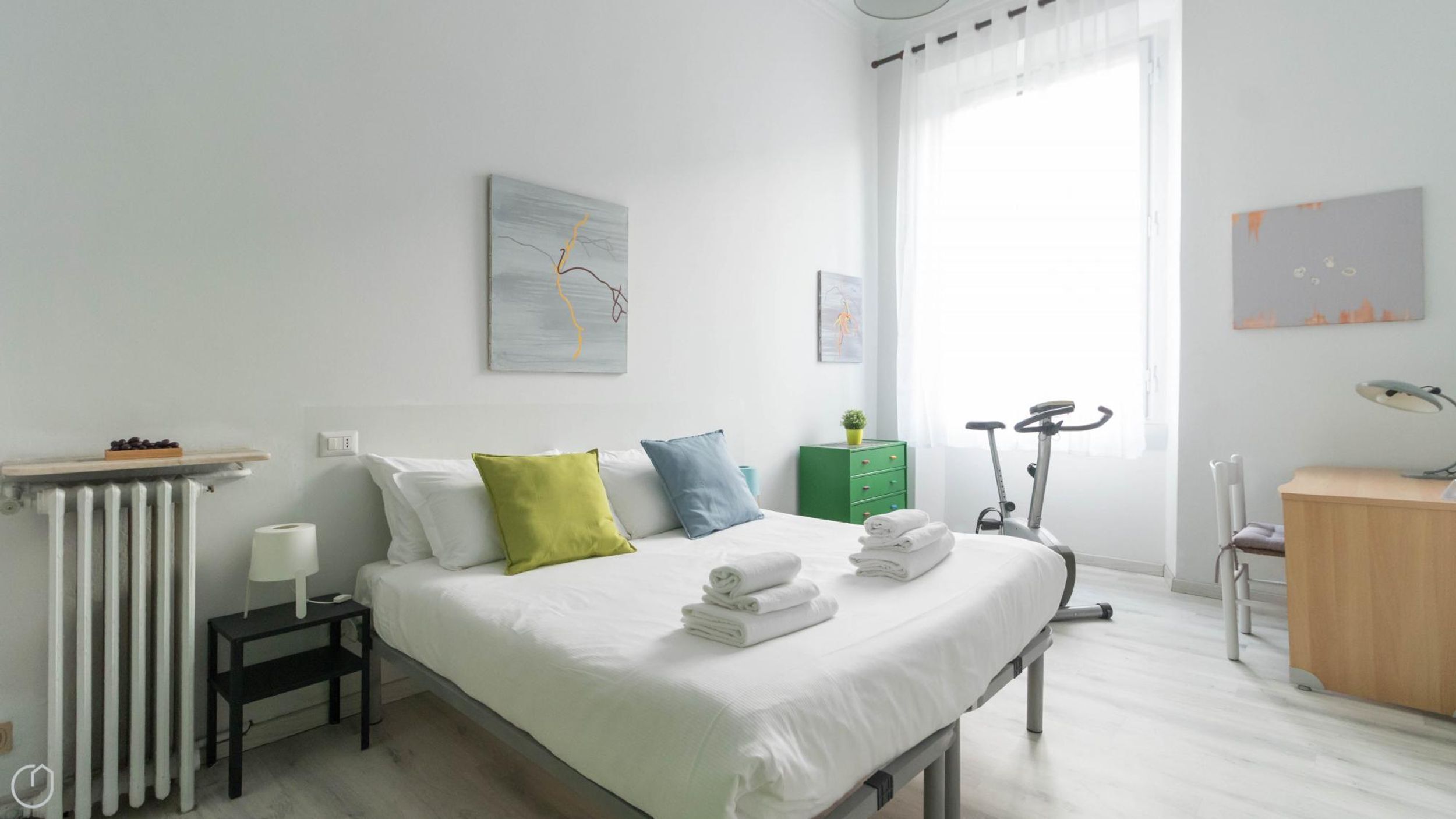Ein modernes Schlafzimmer mit einem Bett, Kissen, einer Heizung, einem Schreibtisch, einem Stuhl und einem Fahrrad.
