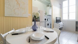 A dining area with a round table set for four, a vase with flowers, and a kitchen in the background. - Piazza Lima 1 (Milan)