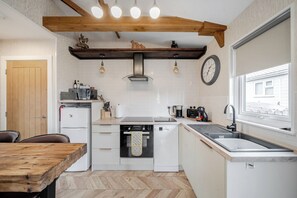 A compact kitchen with a wooden ceiling, white cabinetry, a built-in oven, and a window with a view.